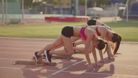 Three-young-women-in-the-stadium-on-the-start-line-in-blocks-start-in-the-race-in-slow-motion